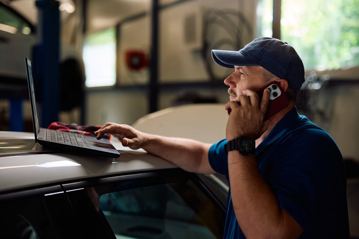 Car mechanic analyzing vehicle diagnostics on a laptop while on a call